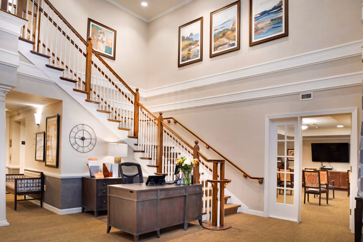 Bright interior lobby with a wooden staircase, reception desk, seating area, and framed artwork on the walls.