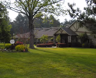 A single-story building with a sloped roof surrounded by trees and a well-maintained lawn, with a sign near the entrance indicating the facility name.