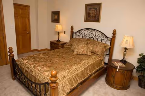 A bedroom with an ornate metal bed frame, two nightstands, lamps, and framed art.