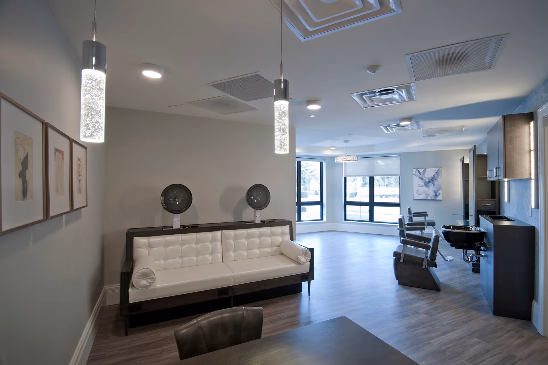 Bright modern interior salon and lounge area with a white tufted bench, salon chairs, hair-washing sinks, and pendant lighting.