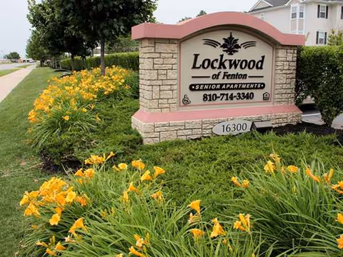 Exterior stone sign for Lockwood of Fenton Senior Apartments with yellow flowers nearby