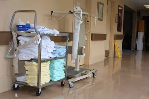 Cleaning cart with folded towels and supplies in a hallway of a senior living facility.