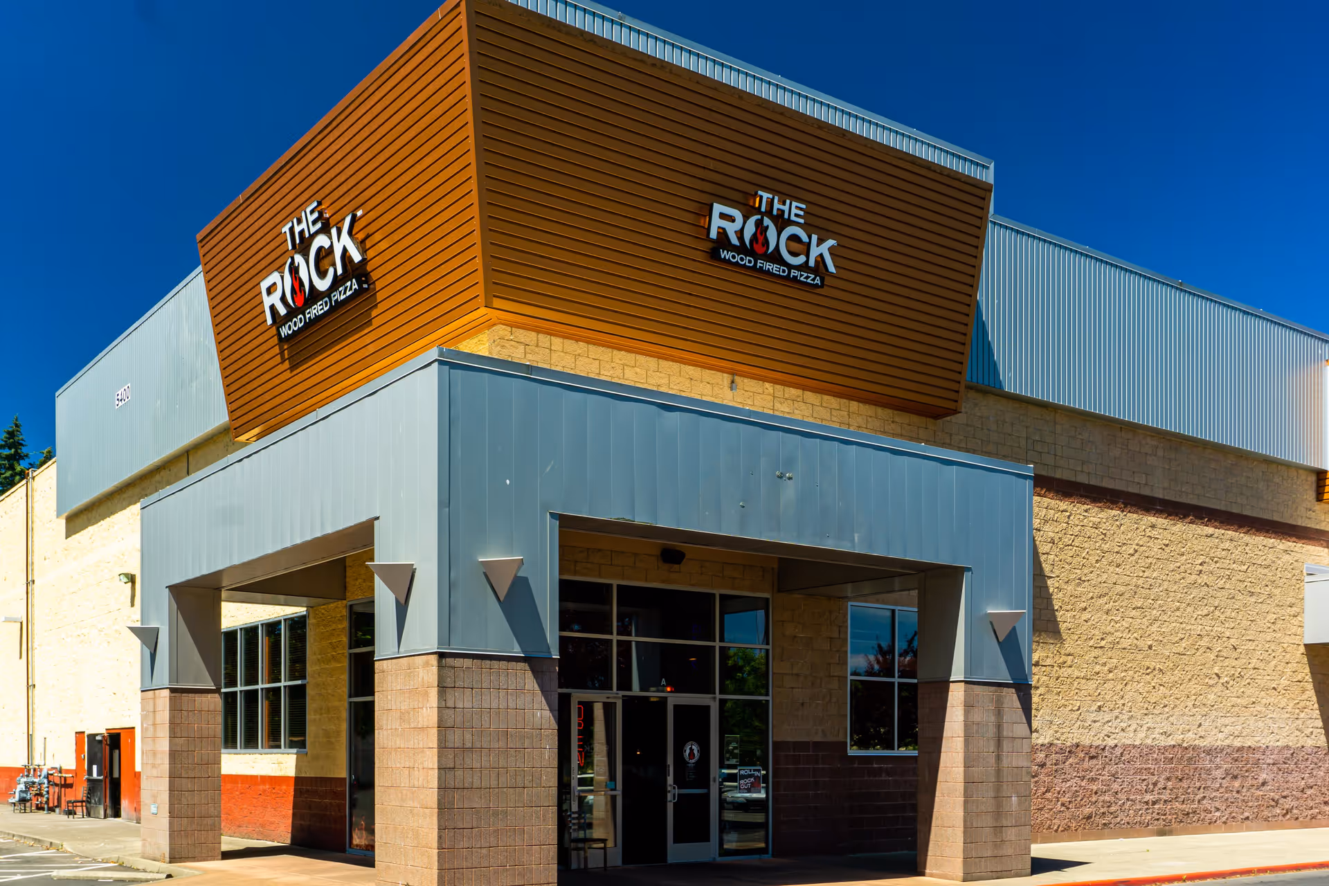 Exterior front entrance of The Rock wood-fired pizza restaurant with a modern facade and large sign.