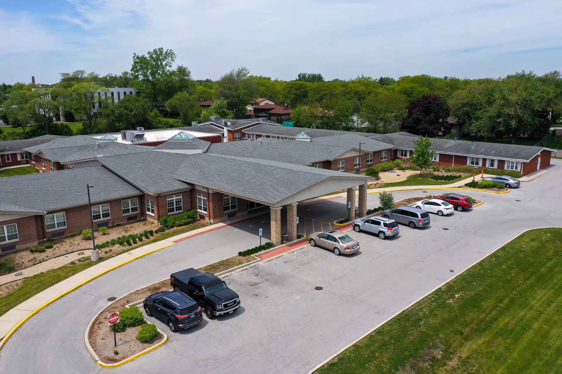 Aerial view of a single-story senior living facility with a covered main entrance and adjacent parking lot.