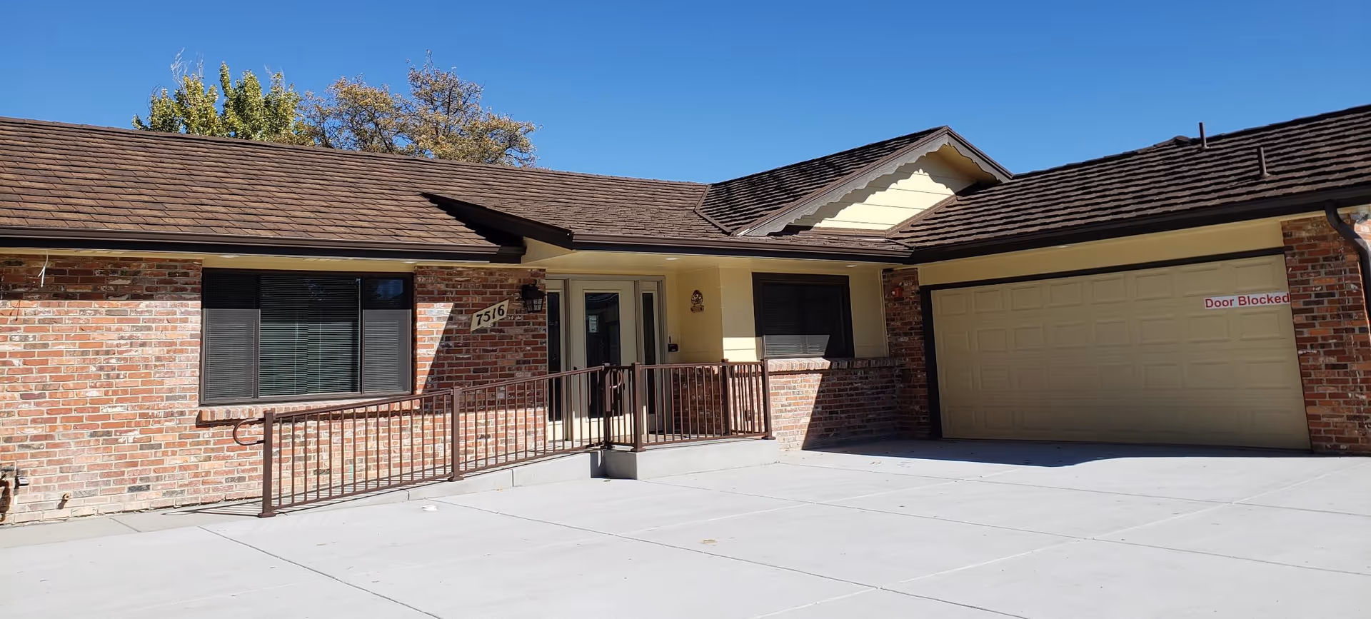 Front exterior of a single-story brick assisted living building with a ramped entrance and attached garage under a clear blue sky.