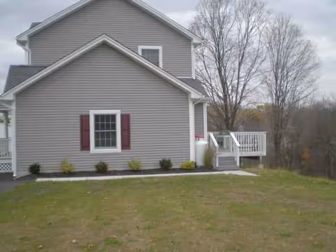 Exterior view of a gray two-story house with a white deck and lawn.