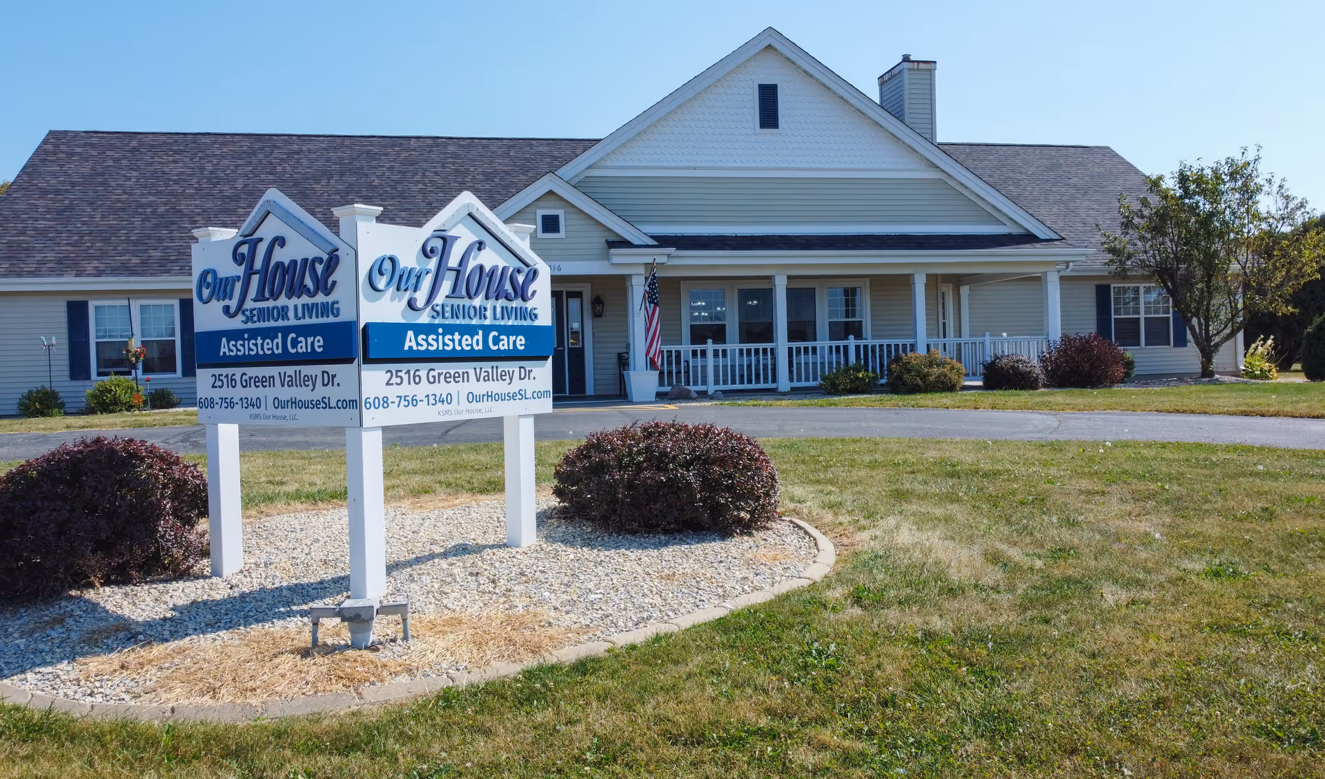 Single-story assisted living building with a front porch and a double sign on the lawn reading 'Our House Senior Living - Assisted Care'.