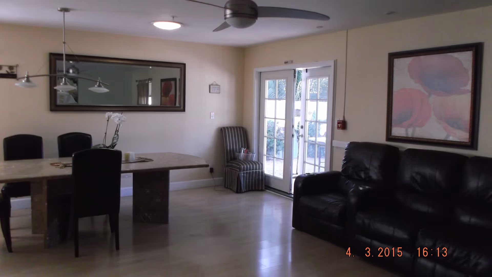 Spacious combined living and dining area with a marble dining table and chairs, black leather sofa, large wall mirror, and glass French doors.