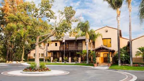 Atria Del Rey exterior shows a two-story Mediterranean-style building with palm trees and a roundabout.