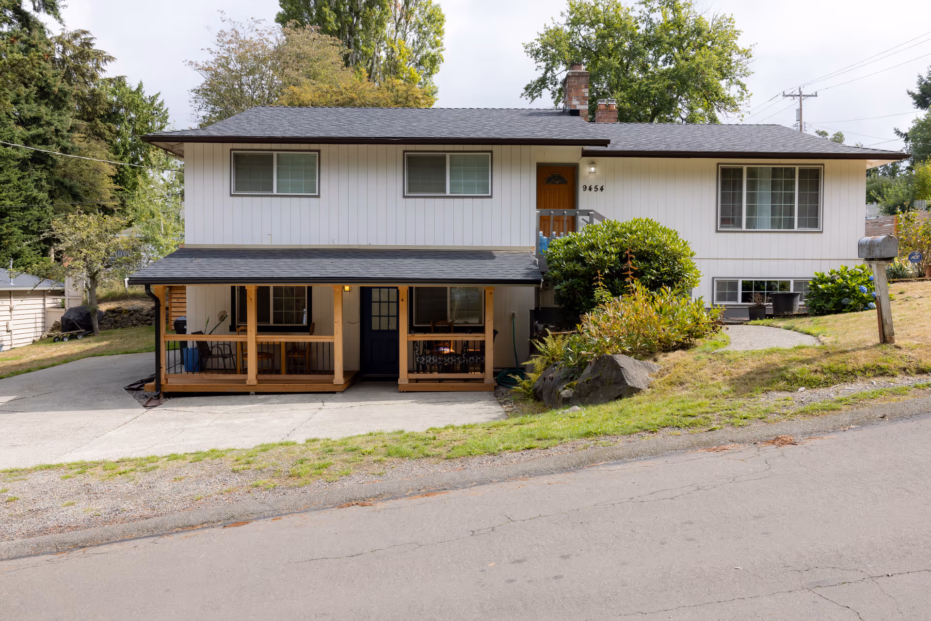 Front view of a two-story suburban house with a covered porch, driveway, and surrounding lawn.
