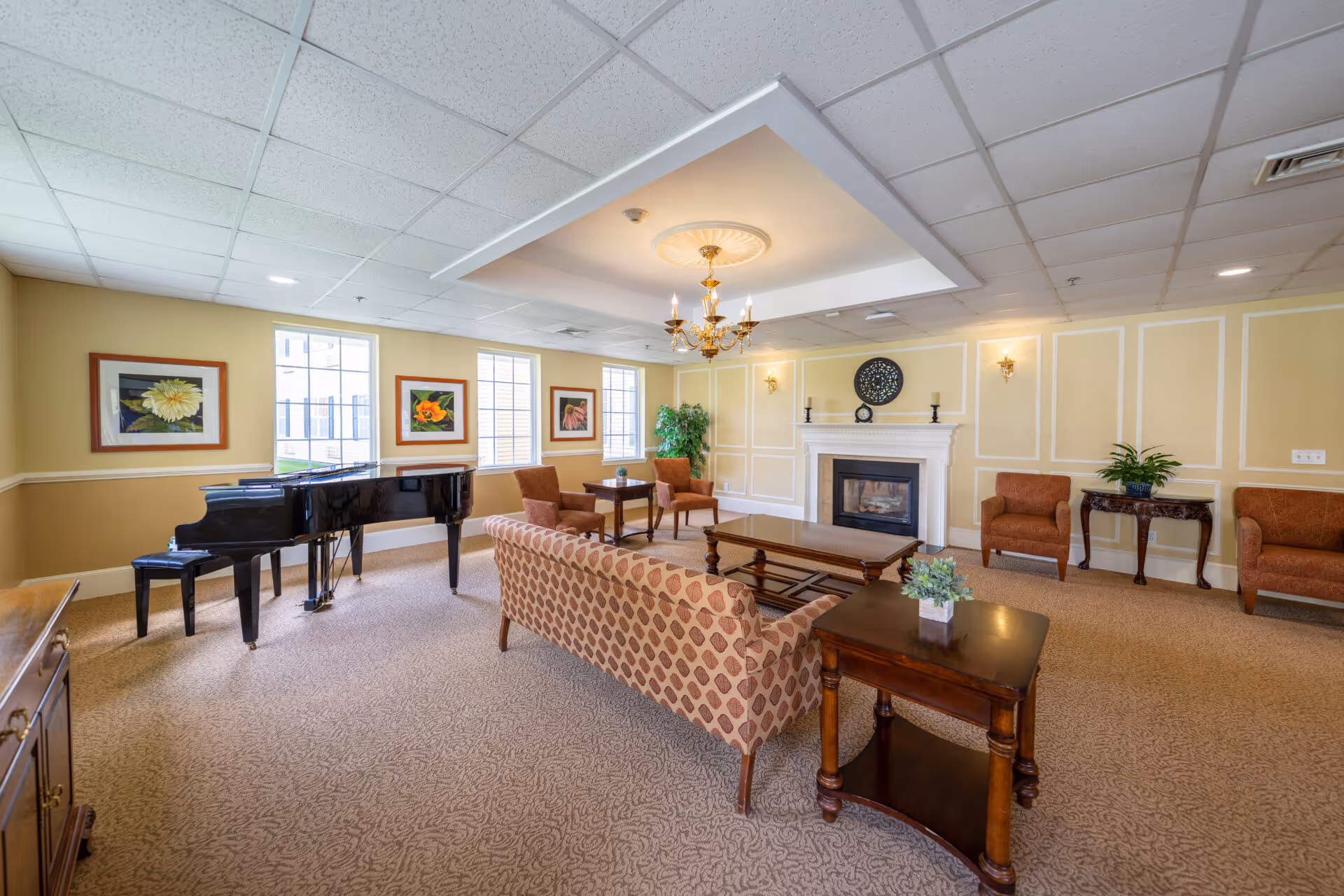 Spacious common room with seating, a grand piano, chandelier, and a fireplace.