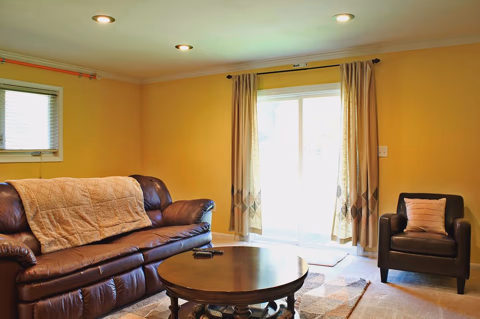 Yellow-walled living room with leather sofa, armchair, coffee table, and sliding glass doors.