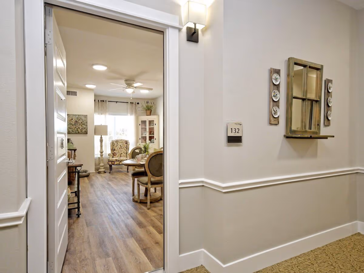 Open doorway numbered 132 revealing a furnished sitting room with chairs, a round table and wood‑look flooring.