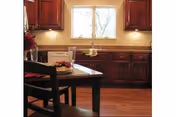 Interior view of a kitchen with wooden cabinets, a window above the sink, and a dining table with chairs in the foreground.