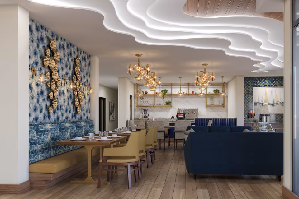 A modern dining and lounge area featuring wooden floors, a long wooden dining table with yellow chairs and blue cushioned bench seating along a wall with blue patterned wallpaper and gold decorative wall sconces. The ceiling has a unique wavy design with integrated lighting. In the background, there are shelves with plants and decorative items, and a coffee station. Blue sofas are arranged in the lounge area to the right.