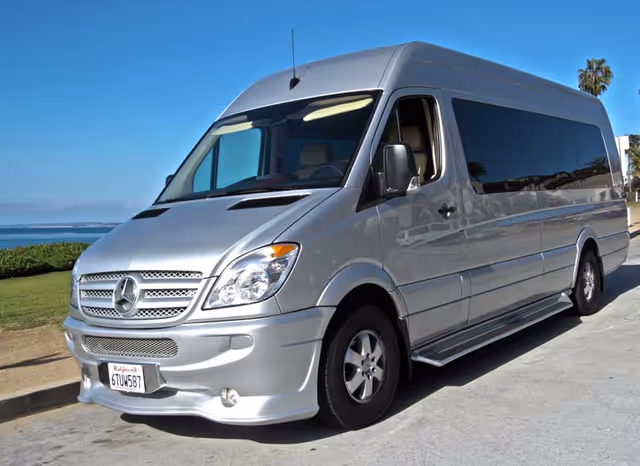 Silver Mercedes-Benz passenger van parked on a coastal road with the ocean in the background.