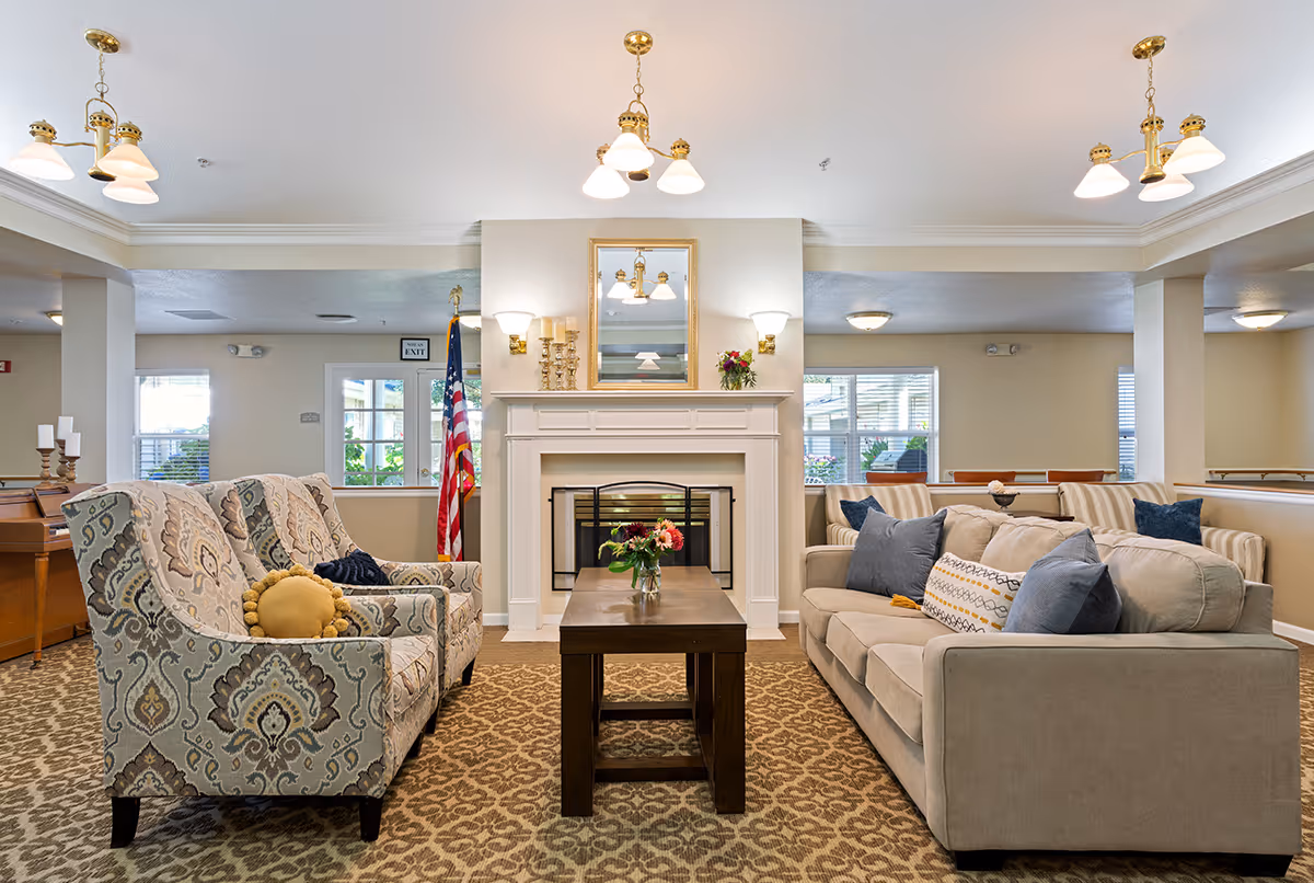 A bright communal living room with patterned armchairs and a sofa facing a coffee table and a fireplace.