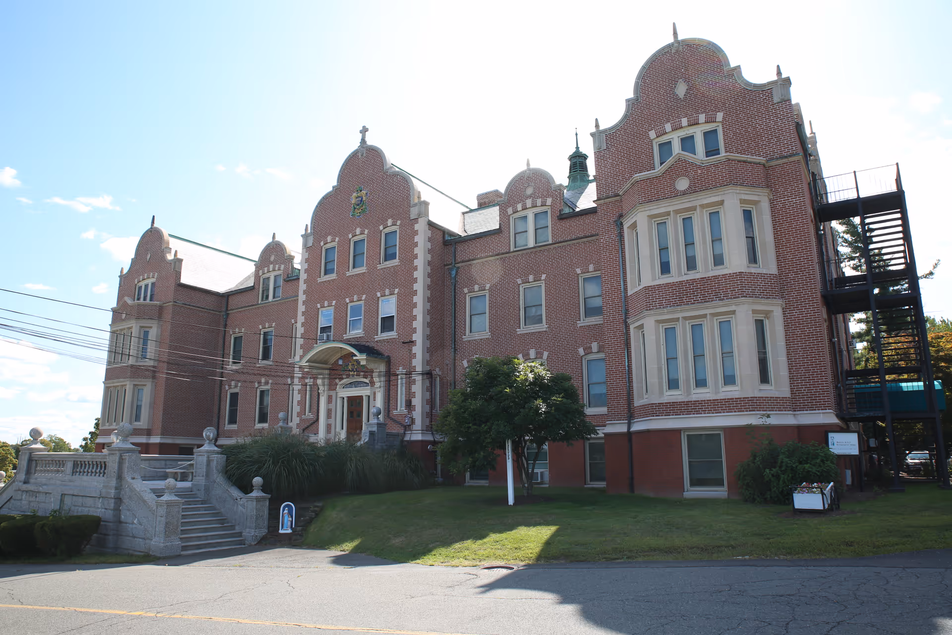 Ornate red-brick building with decorative gables, front steps, and a grassy lawn.