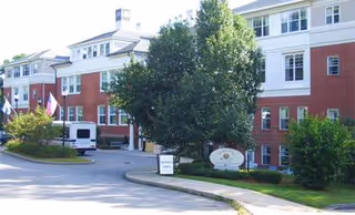 Exterior view of Academy Point at Mystic residential building with trees, driveway, and a sign.