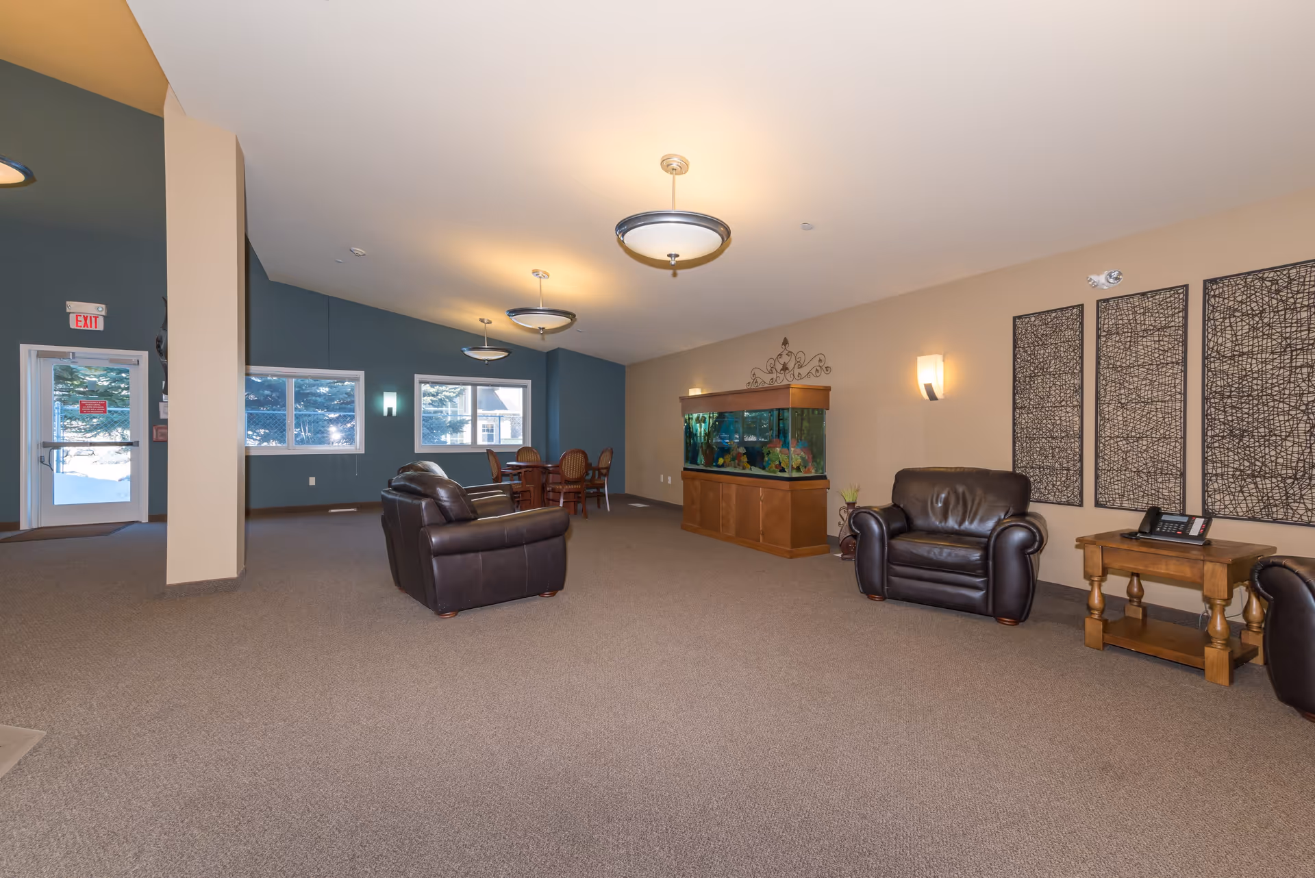 Spacious communal living room with leather chairs, an aquarium, a dining table, and large windows.