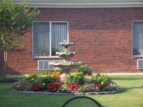 Brick building facade with a garden fountain and colorful flowers in front.
