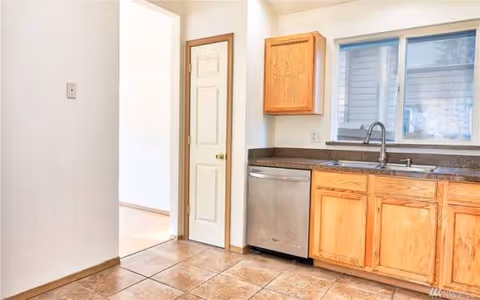 Kitchen area in Saint Joseph Home Care, with wooden cabinets, dishwasher, sink, and tiled floor.