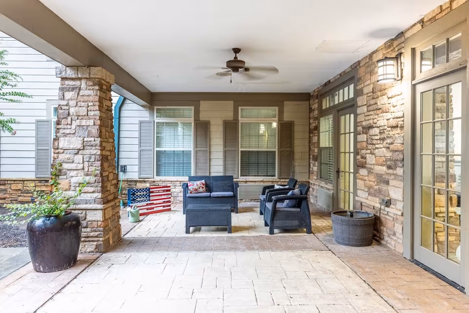 Covered outdoor patio with wicker seating, stone columns, a ceiling fan, potted plants and French doors.