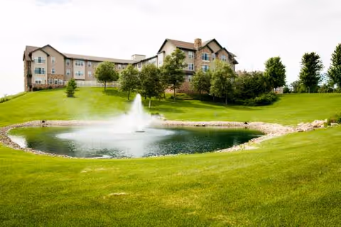 Senior living facility Eagle Crest North sits behind a pond with a fountain and manicured lawn.