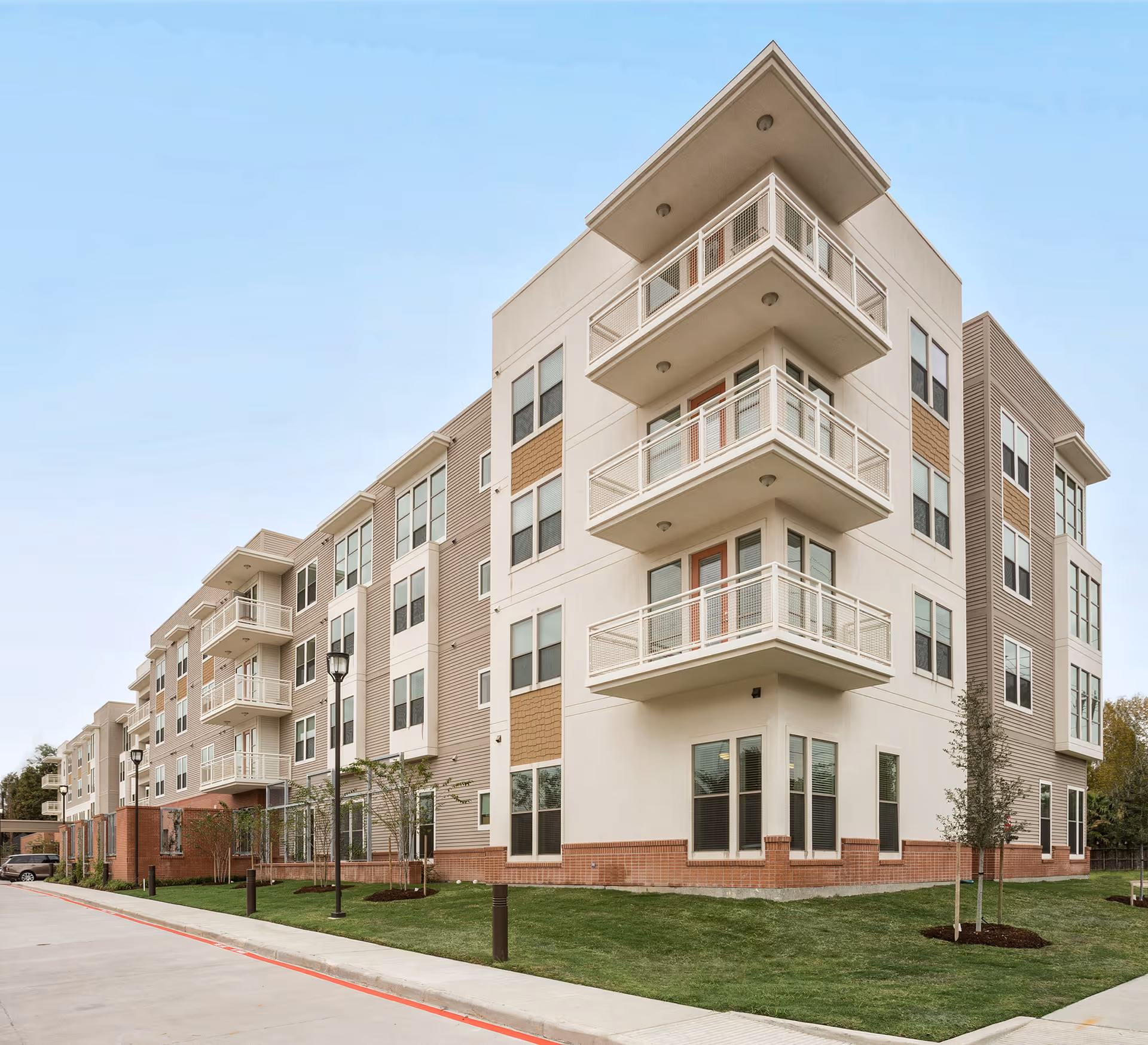 Exterior view of a modern four-story apartment building with balconies, many windows, and landscaped lawn.