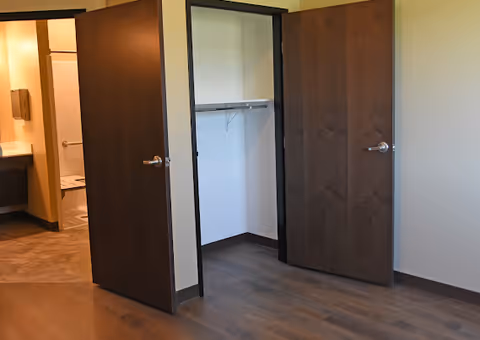 Empty room with an open closet and wooden doors, one leading to a bathroom area.