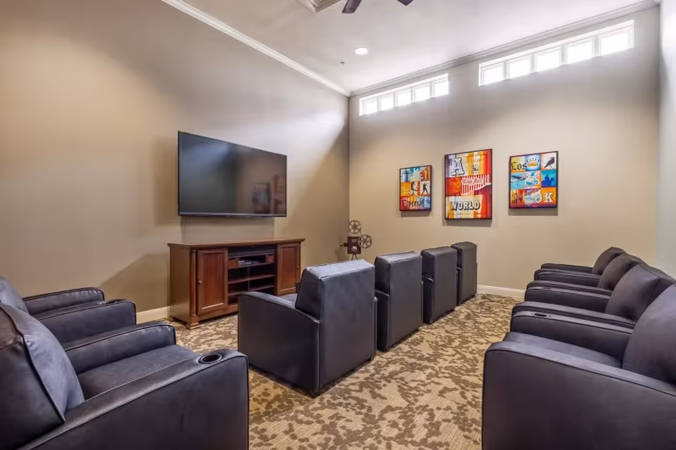 Small screening room with rows of black recliner chairs facing a wall-mounted TV and colorful wall art.