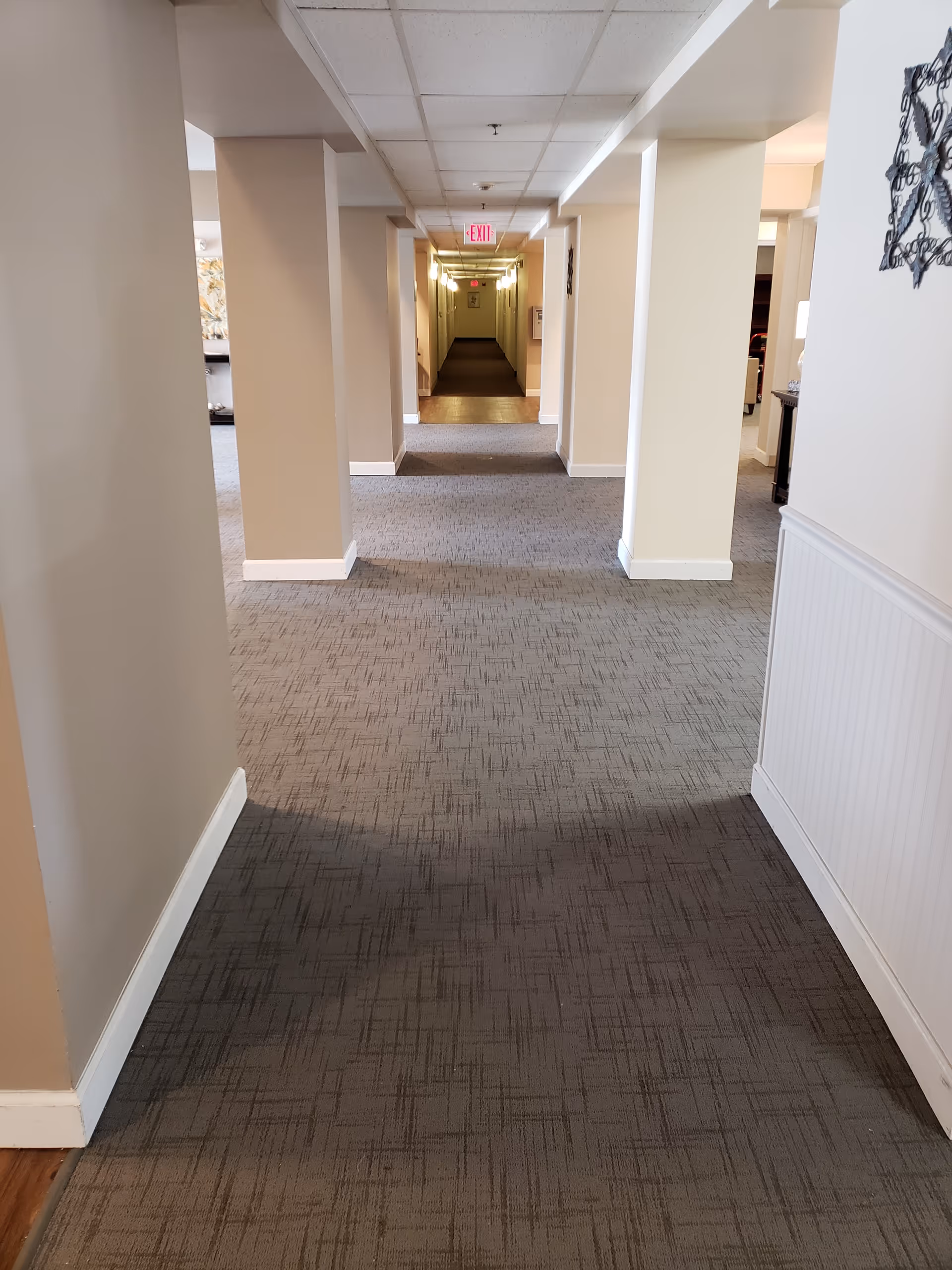 Carpeted interior hallway with columns and a distant EXIT sign at the far end.