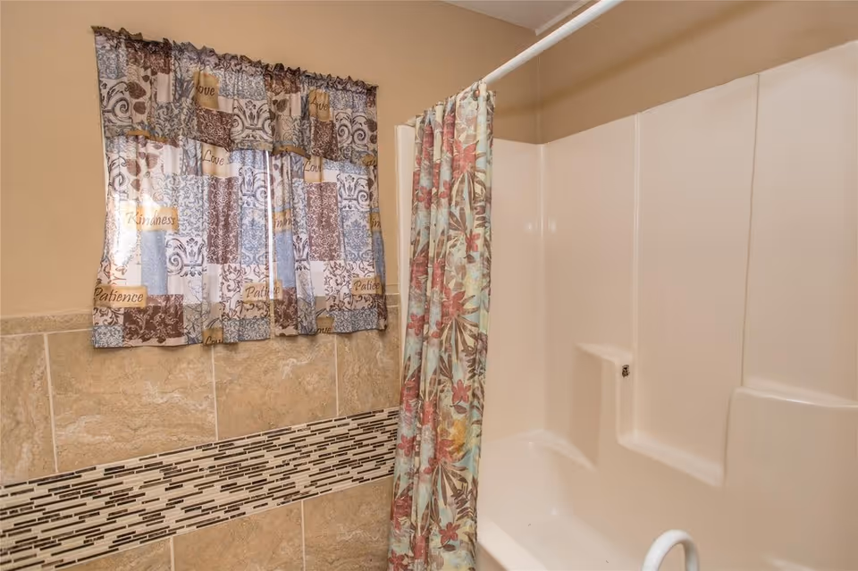 Shower/tub with a floral shower curtain, tiled wall trim and a patterned window curtain.