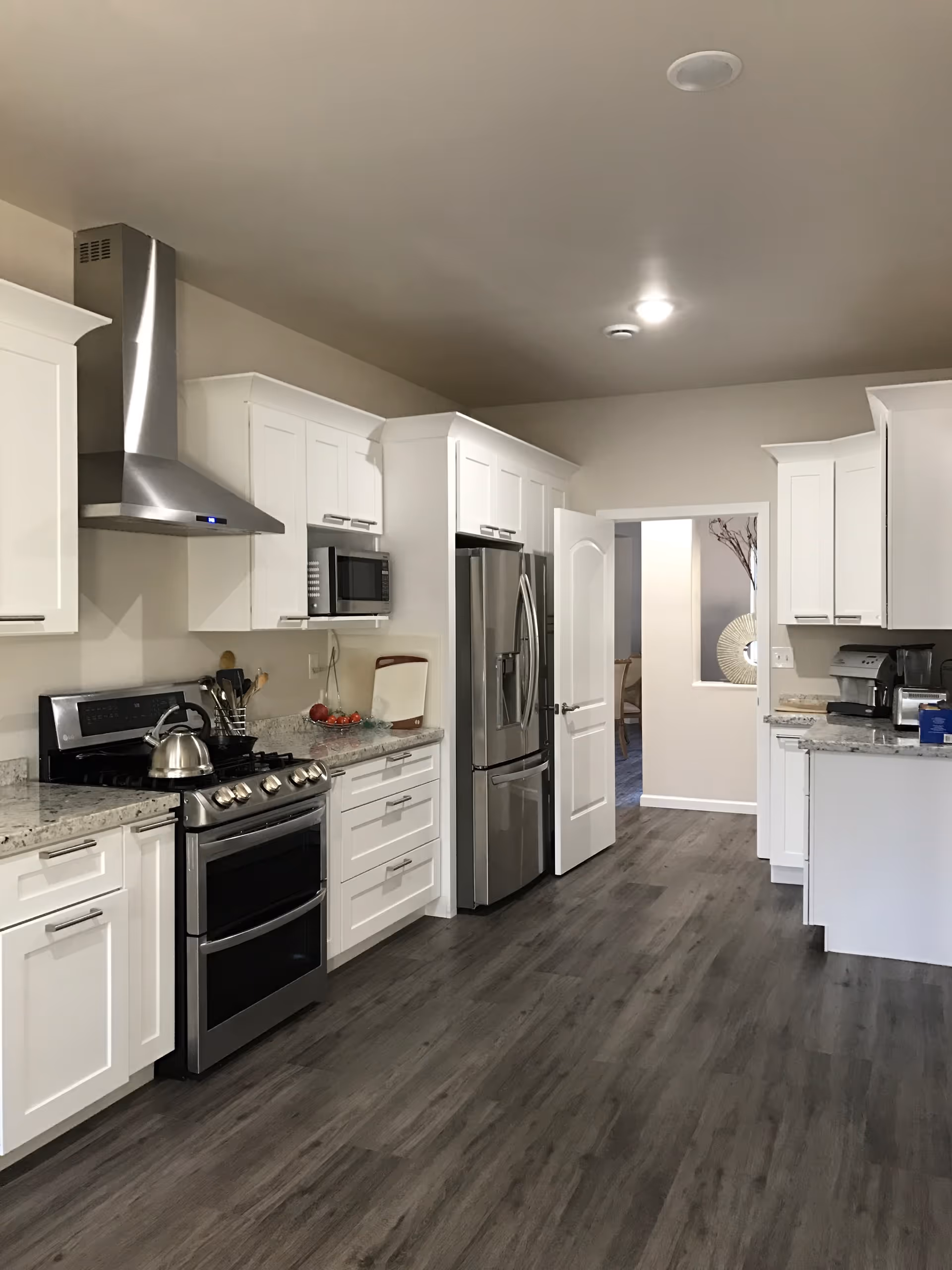 Bright modern kitchen with white cabinets, stainless steel appliances, granite countertops, and gray wood flooring.