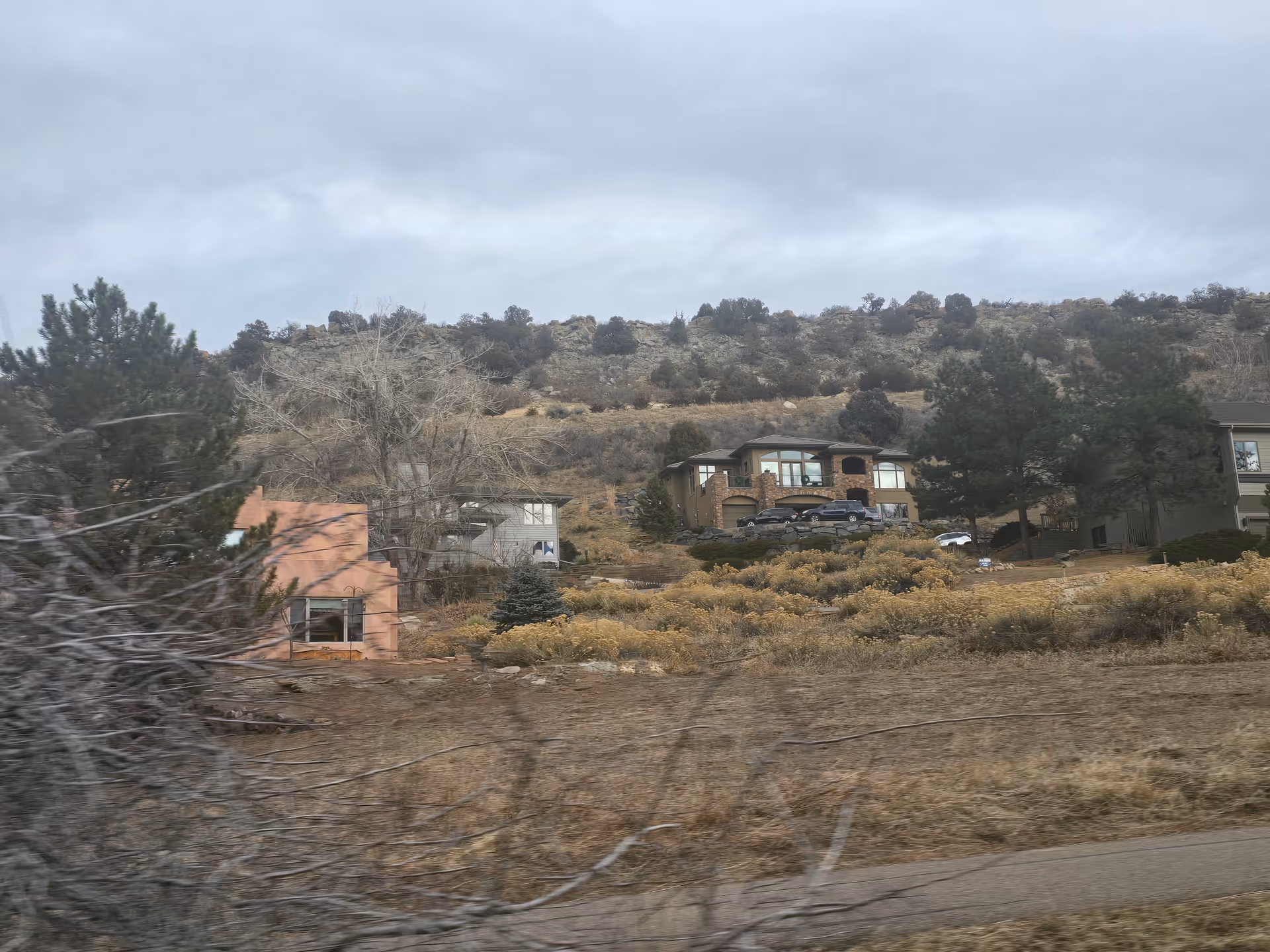 Hillside view showing several houses and dry shrubs under a cloudy sky.