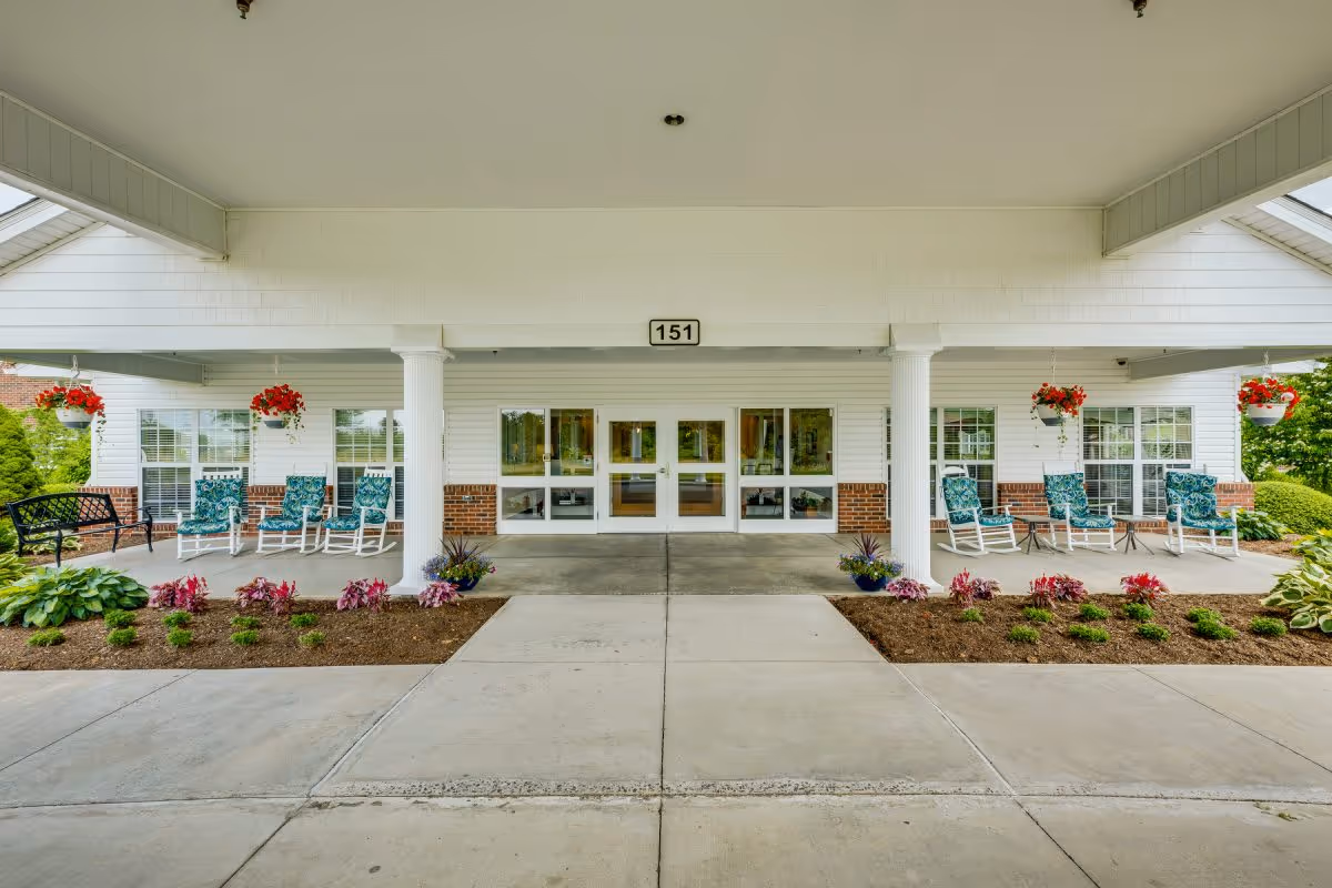 Covered front entrance with white columns, rocking chairs, hanging flower baskets, and double glass doors.