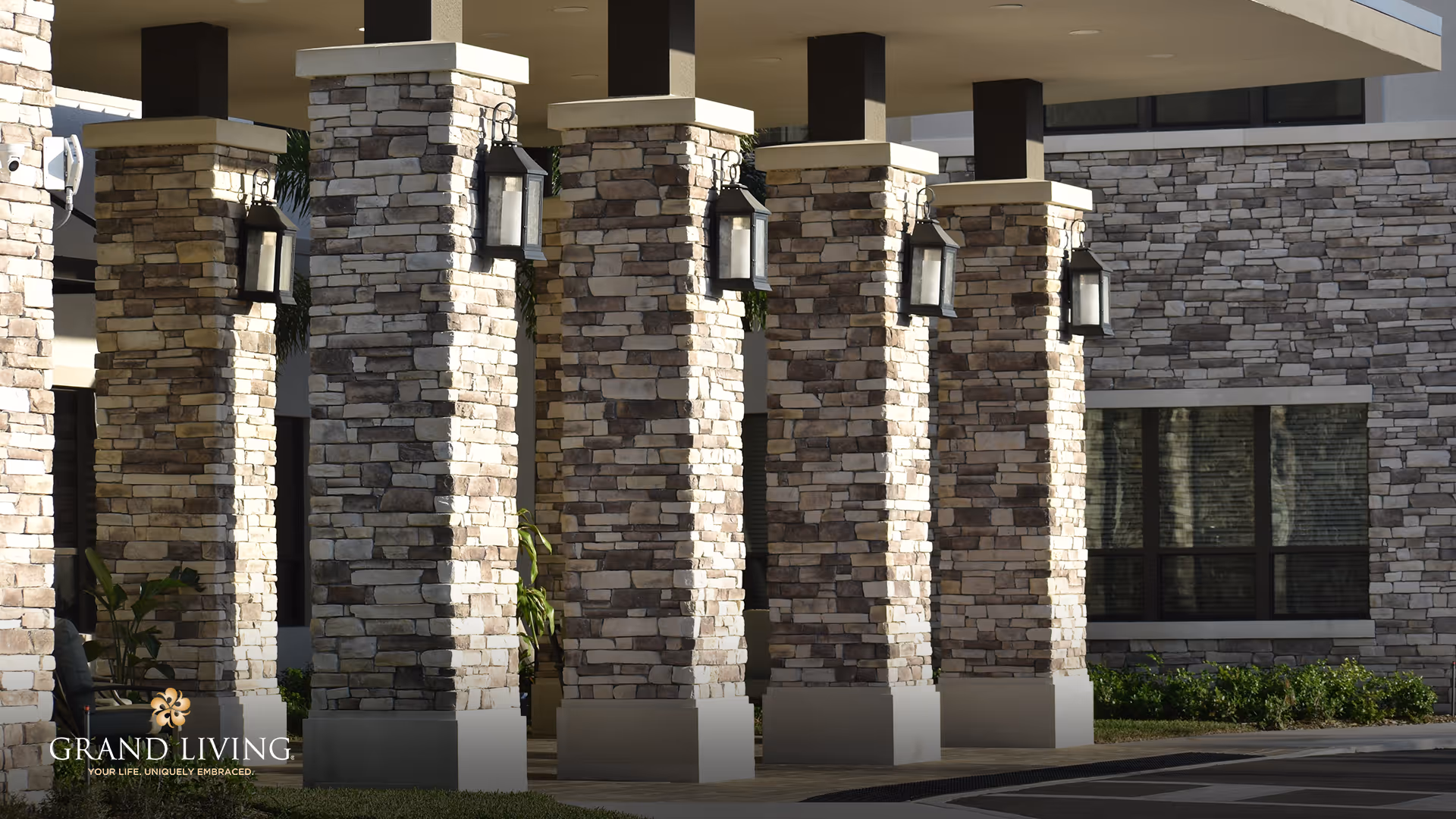 Stone pillars with mounted lantern-style lights at the entrance of a building, with a window and landscaping visible in the background.