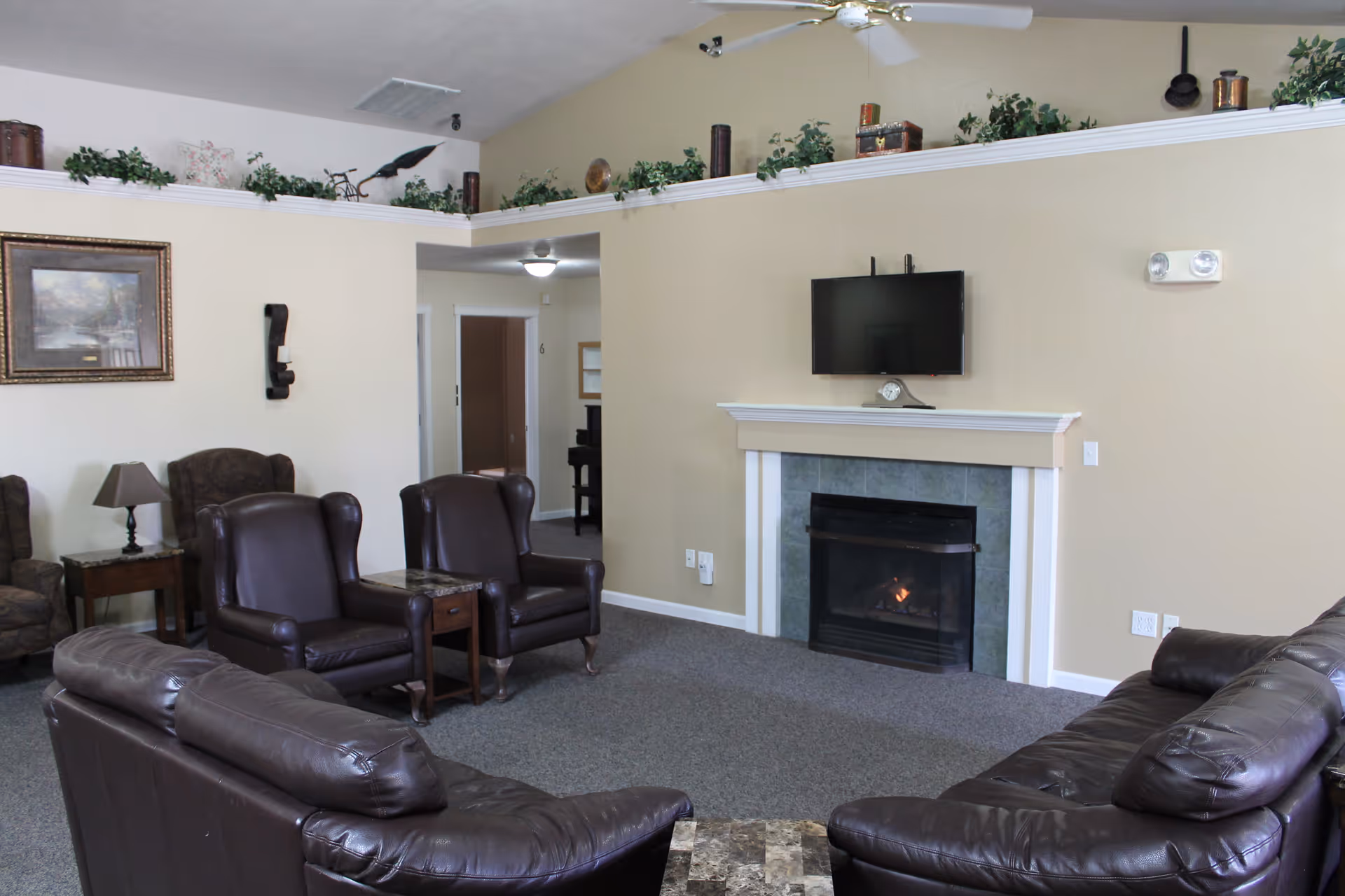 A communal living room with leather sofas and armchairs arranged around a fireplace and wall-mounted TV.