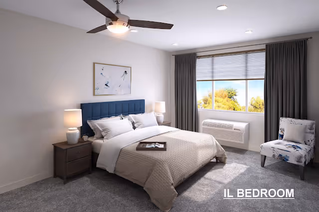 Well-lit modern bedroom with a made bed, upholstered headboard, nightstands with lamps, a ceiling fan, window air conditioner, and an accent chair.