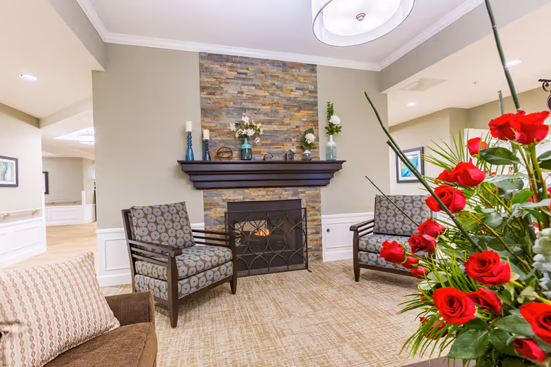 Cozy seating area with two patterned armchairs facing a stone fireplace and a bouquet of red roses in the foreground.