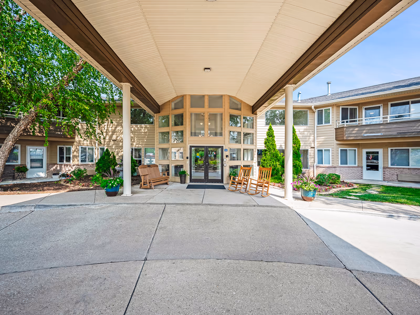 Wide entrance to Holiday Palmer Hills with glass doors, covered drop-off, and rocking chairs outside.