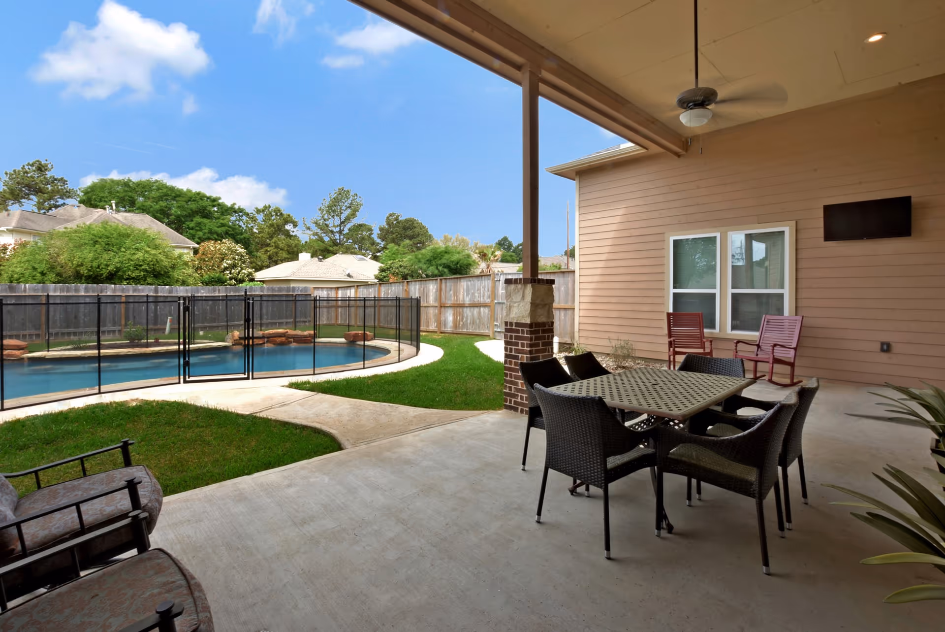 Covered patio with a dining table and chairs overlooking a fenced swimming pool and backyard.