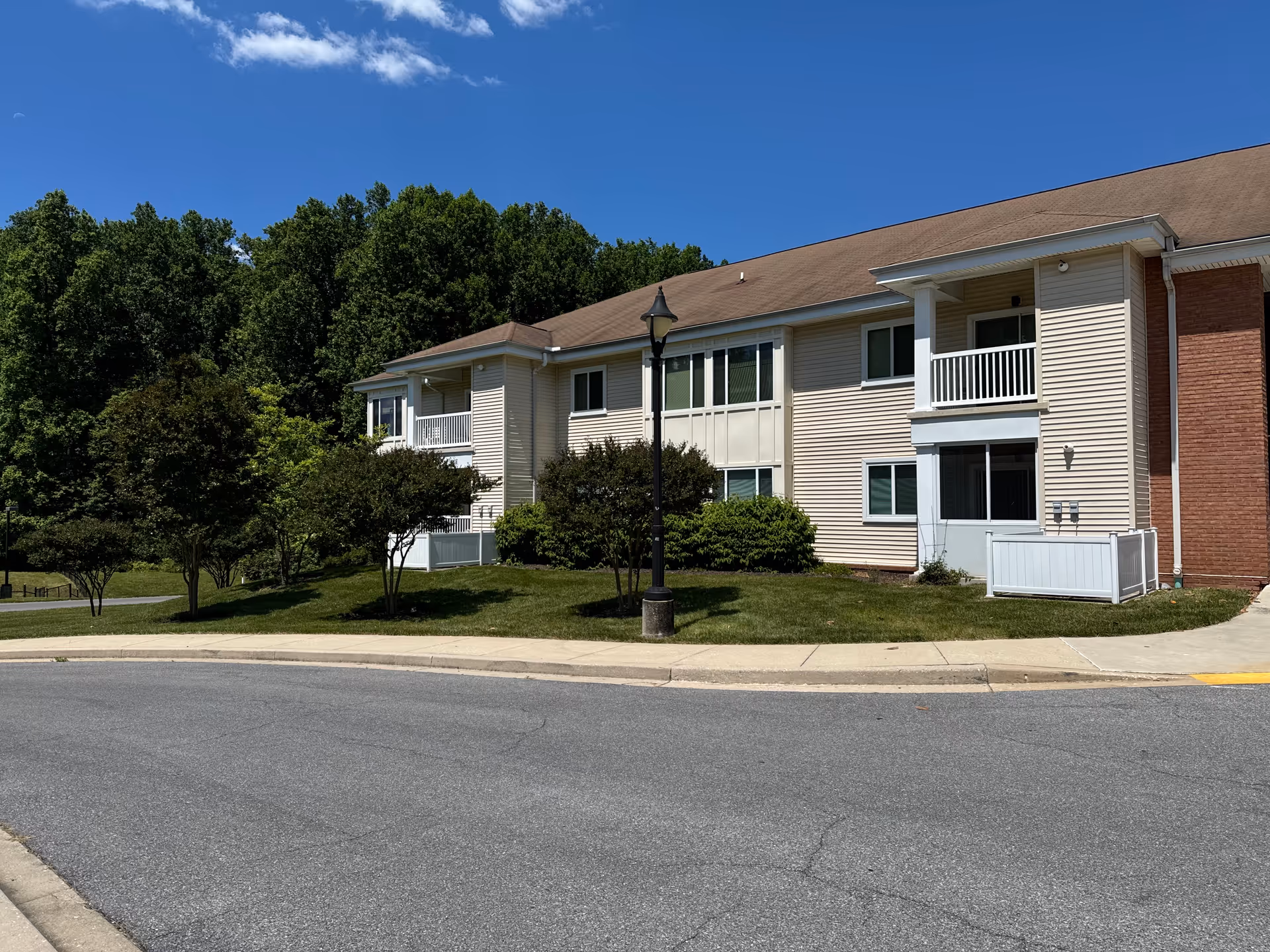 Exterior view shows Heritage at Augsburg senior living building with trees and a street.