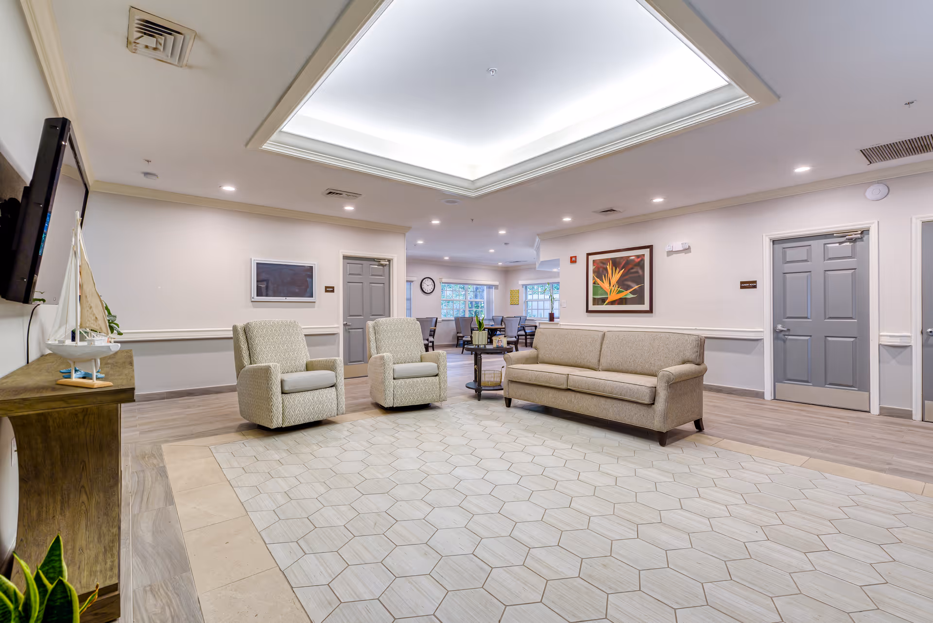 Common seating area in a senior living facility with a sofa, two armchairs, coffee table, and large recessed ceiling light.