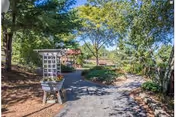 Shaded paved walkway through a landscaped garden with trees, a trellis planter, and benches.