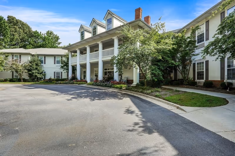 Exterior view of Oaks at Stockbridge senior living facility with a porch, trees, and parking.