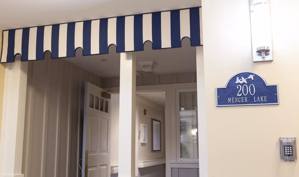 Interior entryway with a blue-and-white striped valance, an open door and a blue plaque reading '200 Mercer Lake'.
