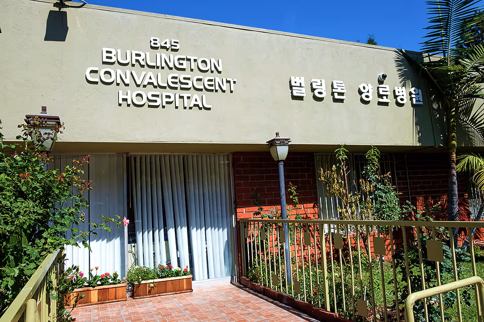 Front entrance of Burlington Convalescent Hospital with large signage above a brick facade, planter boxes, railing and a lamp post.