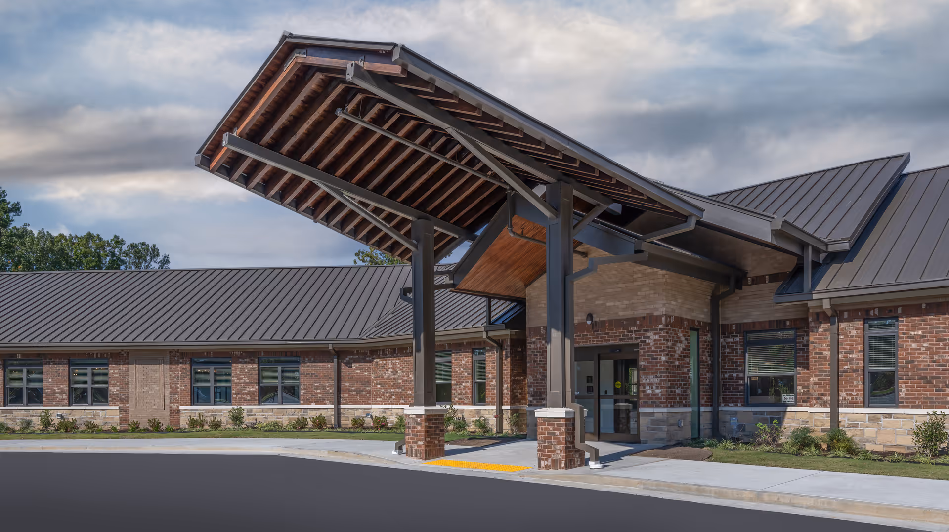 Front entrance of a brick senior living building with a large covered porte-cochere and metal roof.