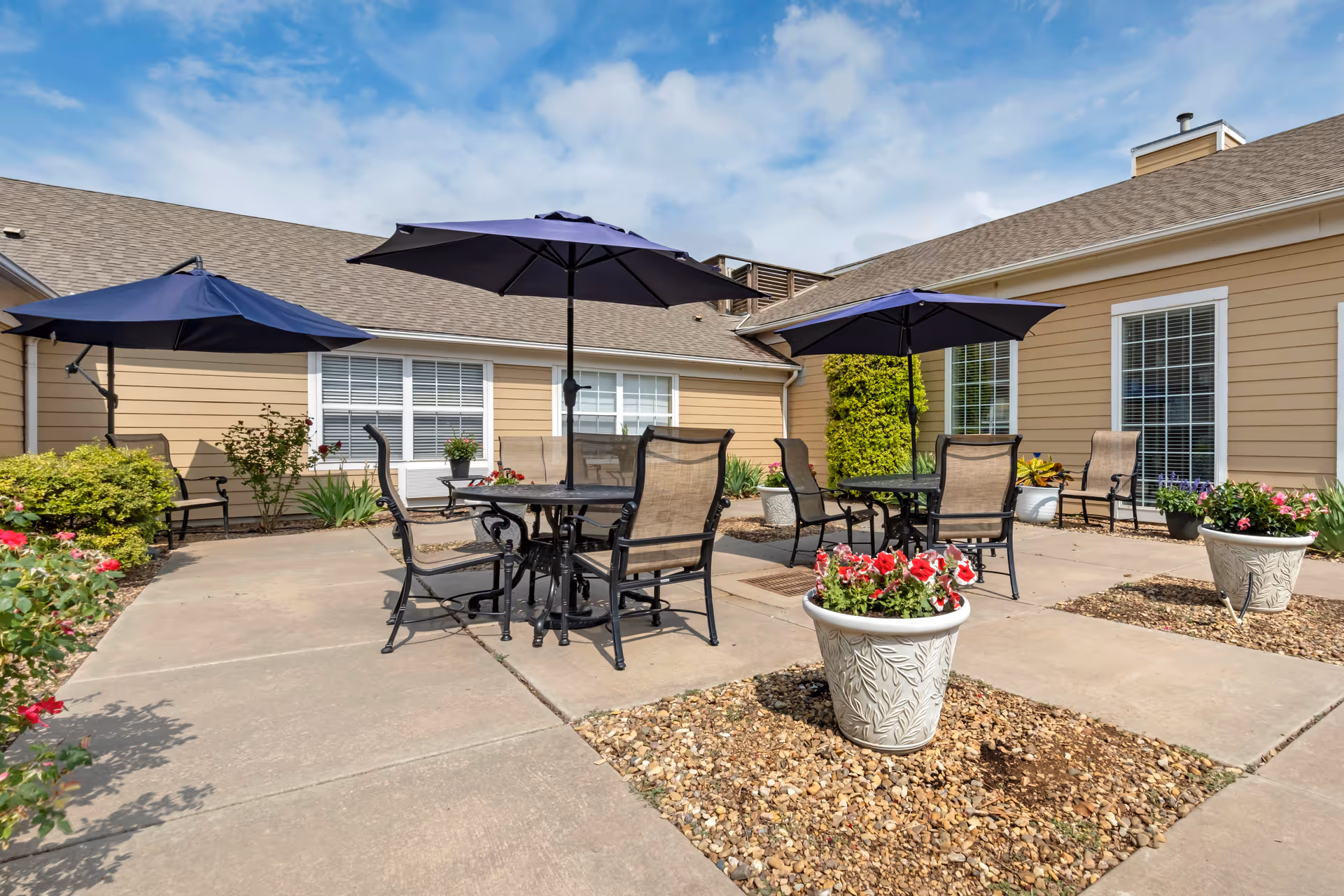Outdoor patio with tables, chairs, umbrellas, and potted flowers by a beige building
